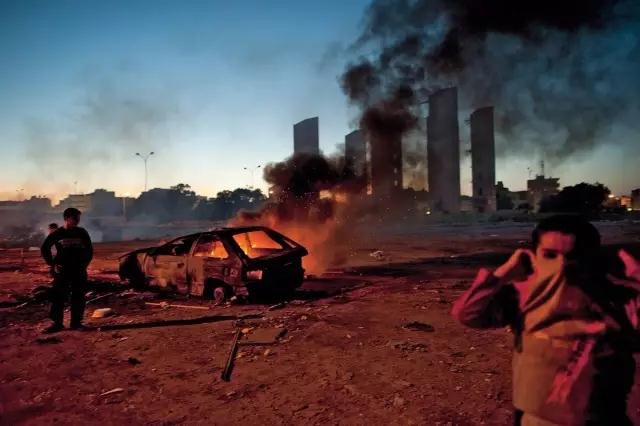 2011 年2 月28 日，利比亚班加西，孩子们在居住区旁燃烧的汽车边玩耍，利比亚战争正在愈演愈烈。